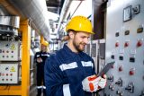 Professional industrial electrician in safety work wear checking power consumption on tablet computer.